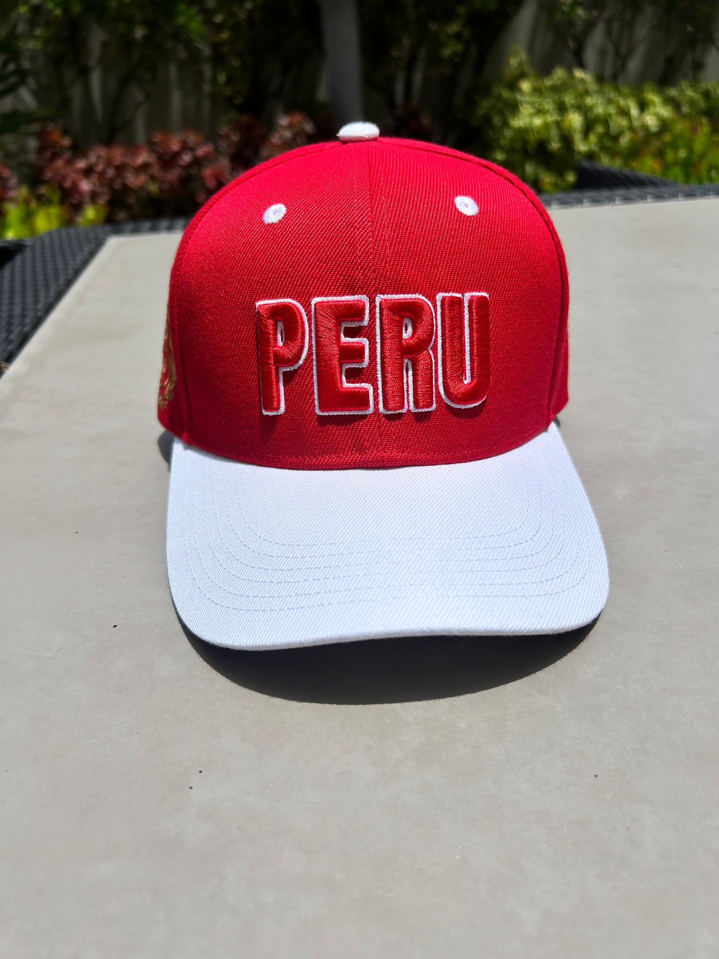 A red and white baseball cap with 'PERU' embroidered in 3D on the front and the Coat of Arms of Peru on the sides, displayed on a flat surface.