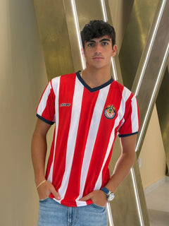 Person wearing a red and white striped sports jersey with a logo, standing against a metallic background.