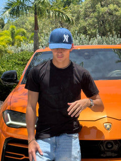 Man wearing the New York denim snapback cap with curved brim, black t-shirt, orange car in background