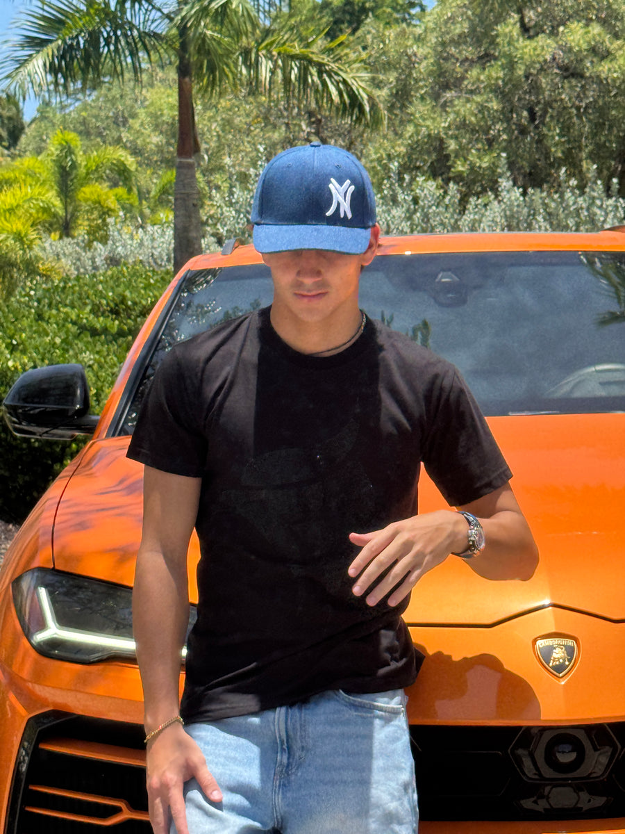 Man wearing the New York denim snapback cap with curved brim, black t-shirt, orange car in background