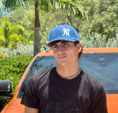 Close-up of man wearing the New York denim snapback cap, black t-shirt, orange car in background
