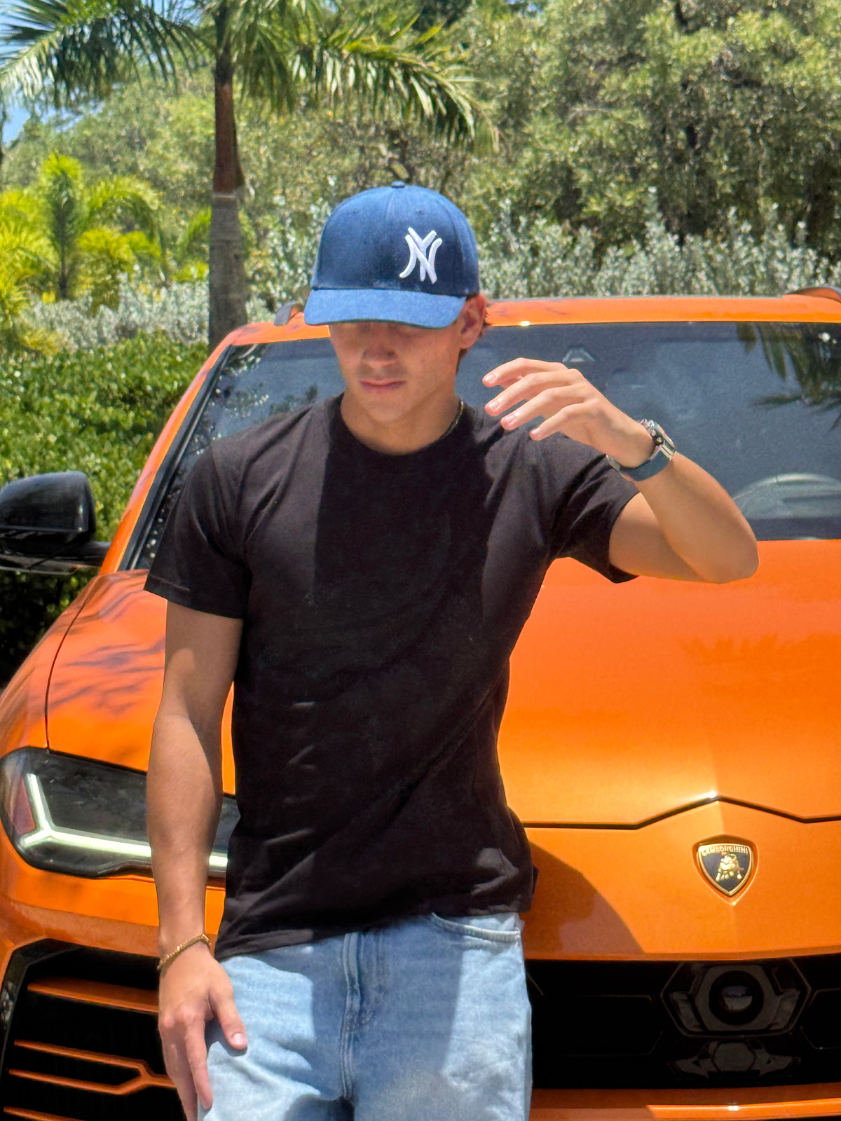 Man adjusting the New York denim snapback cap, front view, black t-shirt, orange car in background