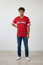 Person wearing a red Panama baseball jersey with blue jeans and white sneakers on a plain background