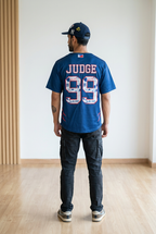 Person wearing a blue t-shirt with 'Judge 99' printed on the back, standing in a room with wooden flooring and a white wall.