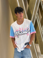 Person wearing a white shirt with colorful text and graphics, standing against a metallic background.