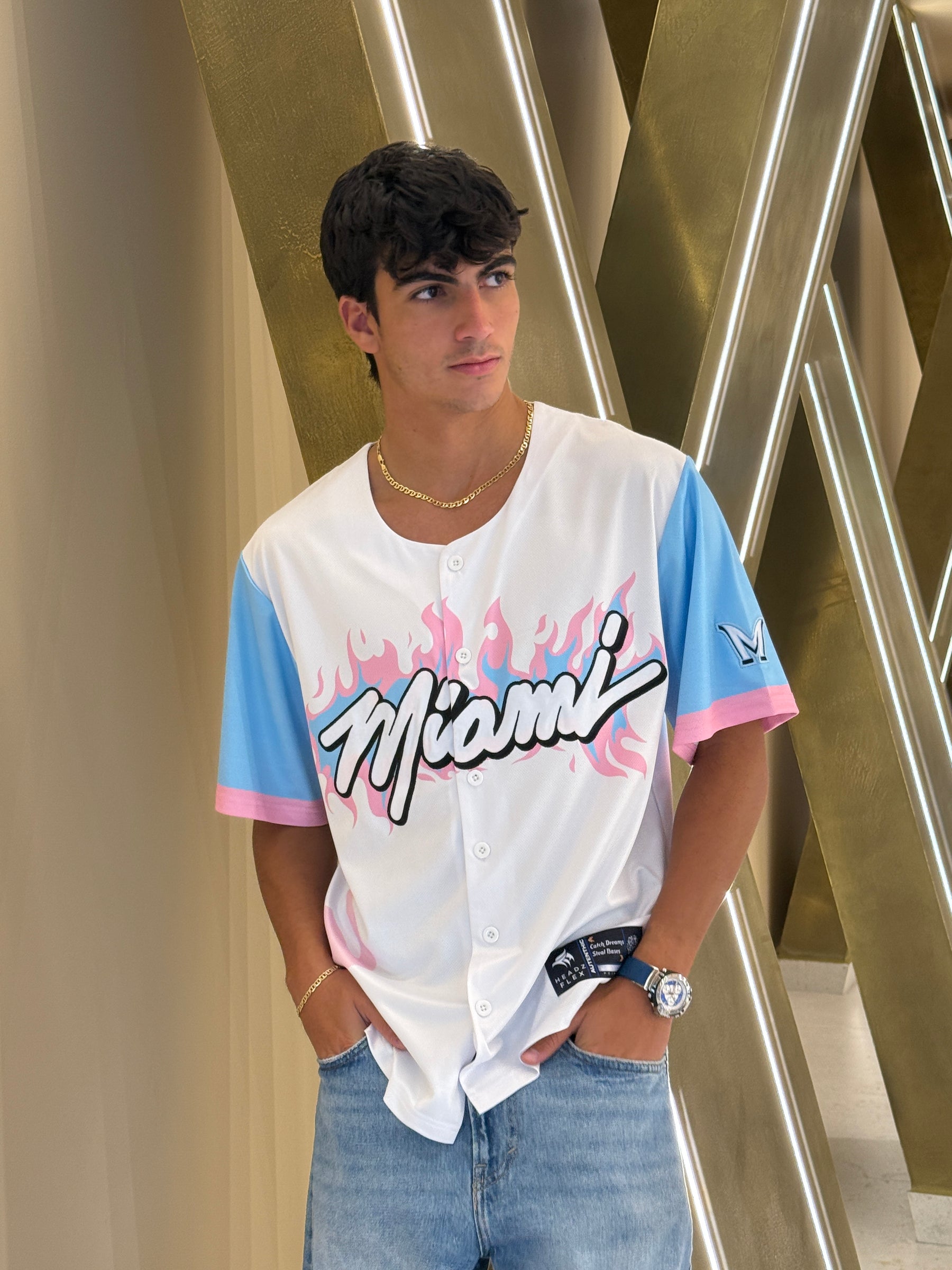Person wearing a white shirt with colorful text and graphics, standing against a metallic background.