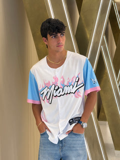 Person wearing a white shirt with colorful text and graphics, standing against a metallic background.