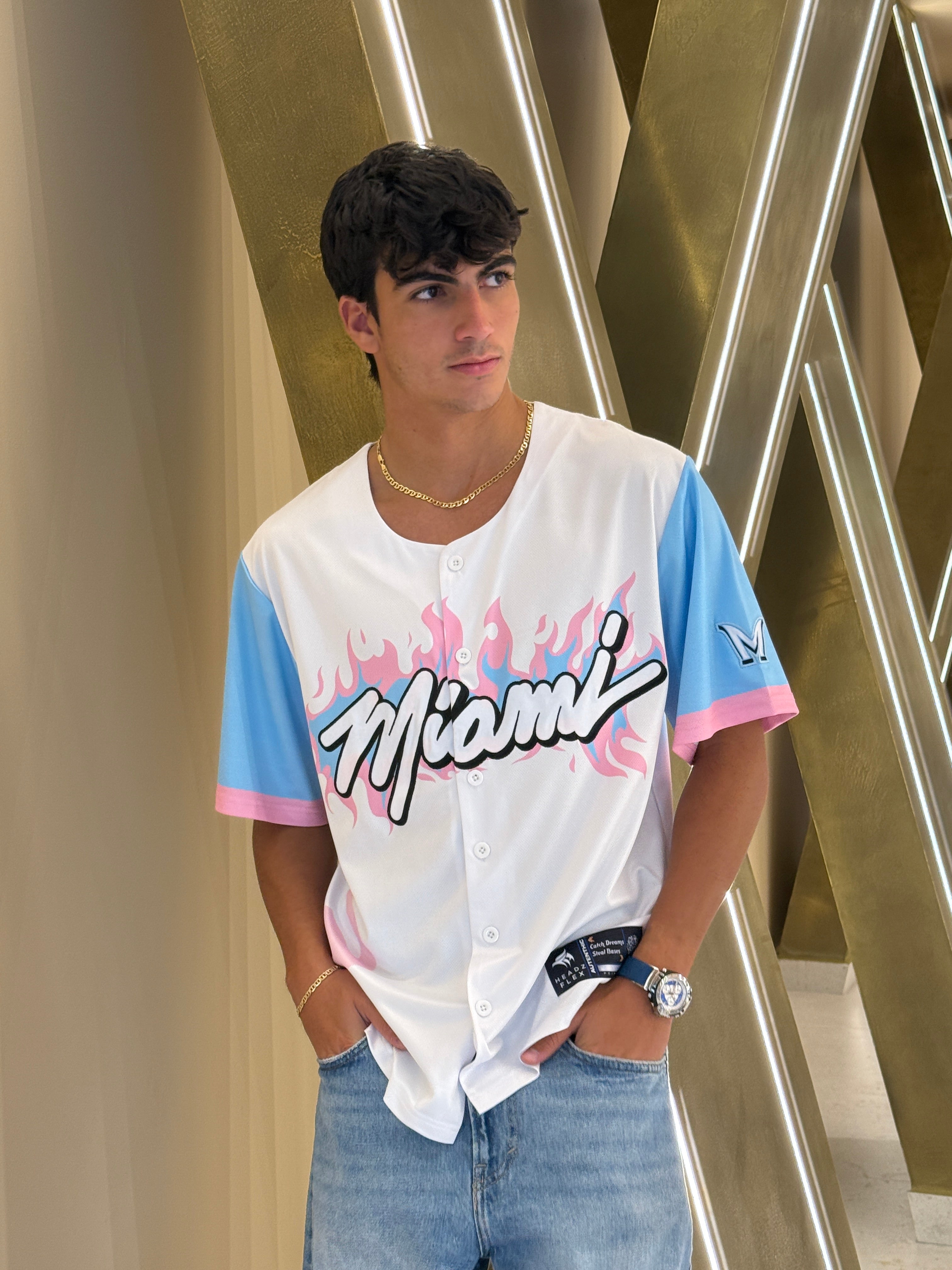 Person wearing a white shirt with colorful text and graphics, standing against a metallic background.