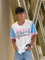 Person wearing a white shirt with colorful text and graphics, standing against a metallic background.