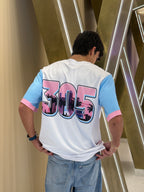 Person wearing a white t-shirt with colorful text design, standing against a modern architectural background.