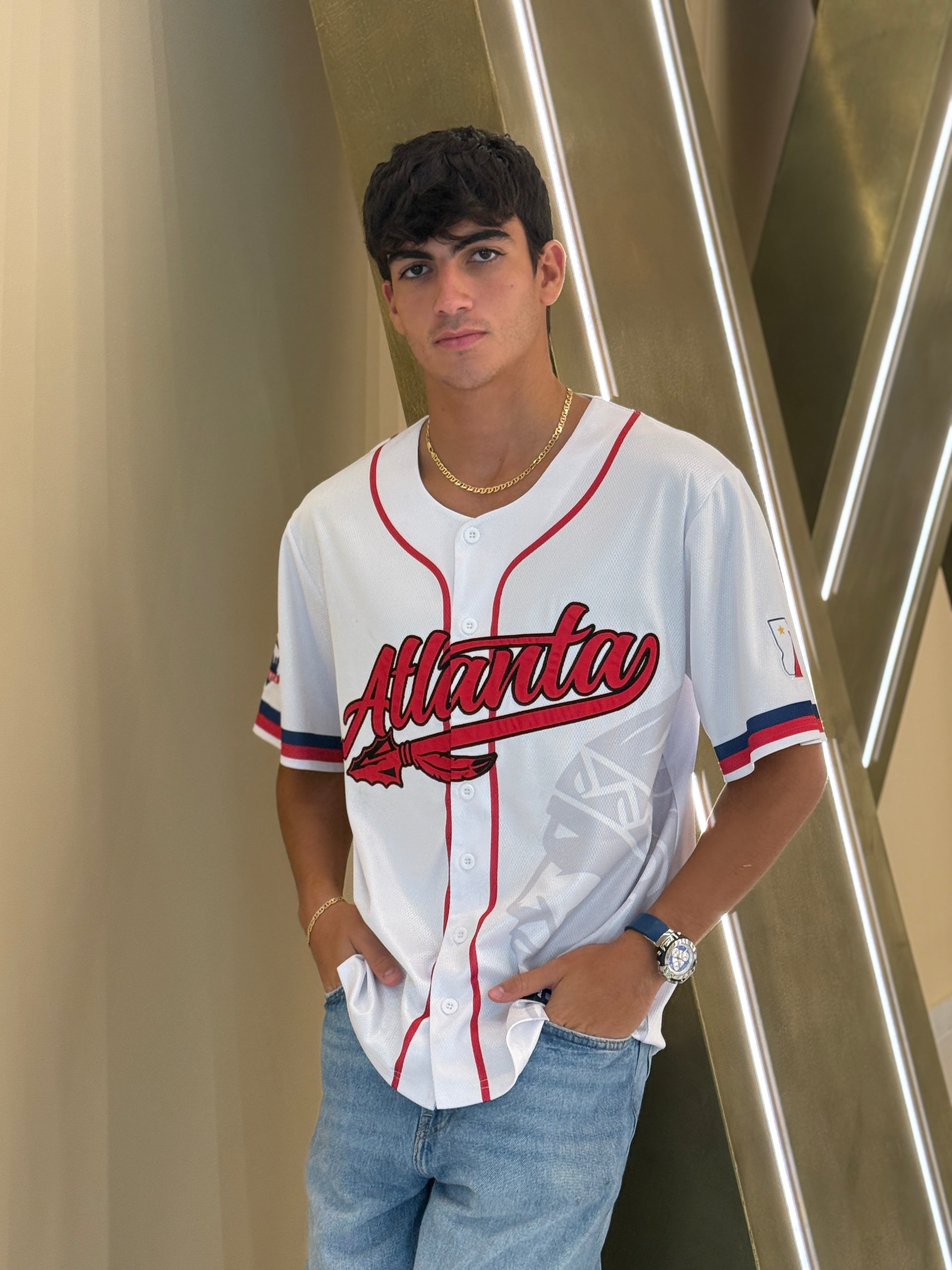 Atlanta baseball jersey 13 - Person wearing a white baseball jersey with 'Atlanta' printed on it, standing against a modern architectural background.