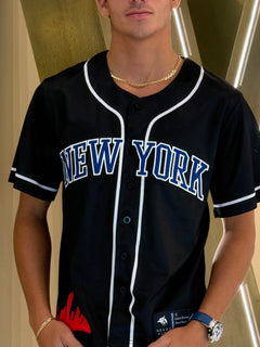 Person wearing a black baseball jersey with 'New York' printed on it, standing against a neutral background.