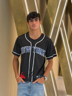 Person wearing a black 'New York' baseball jersey in front of a gold geometric background