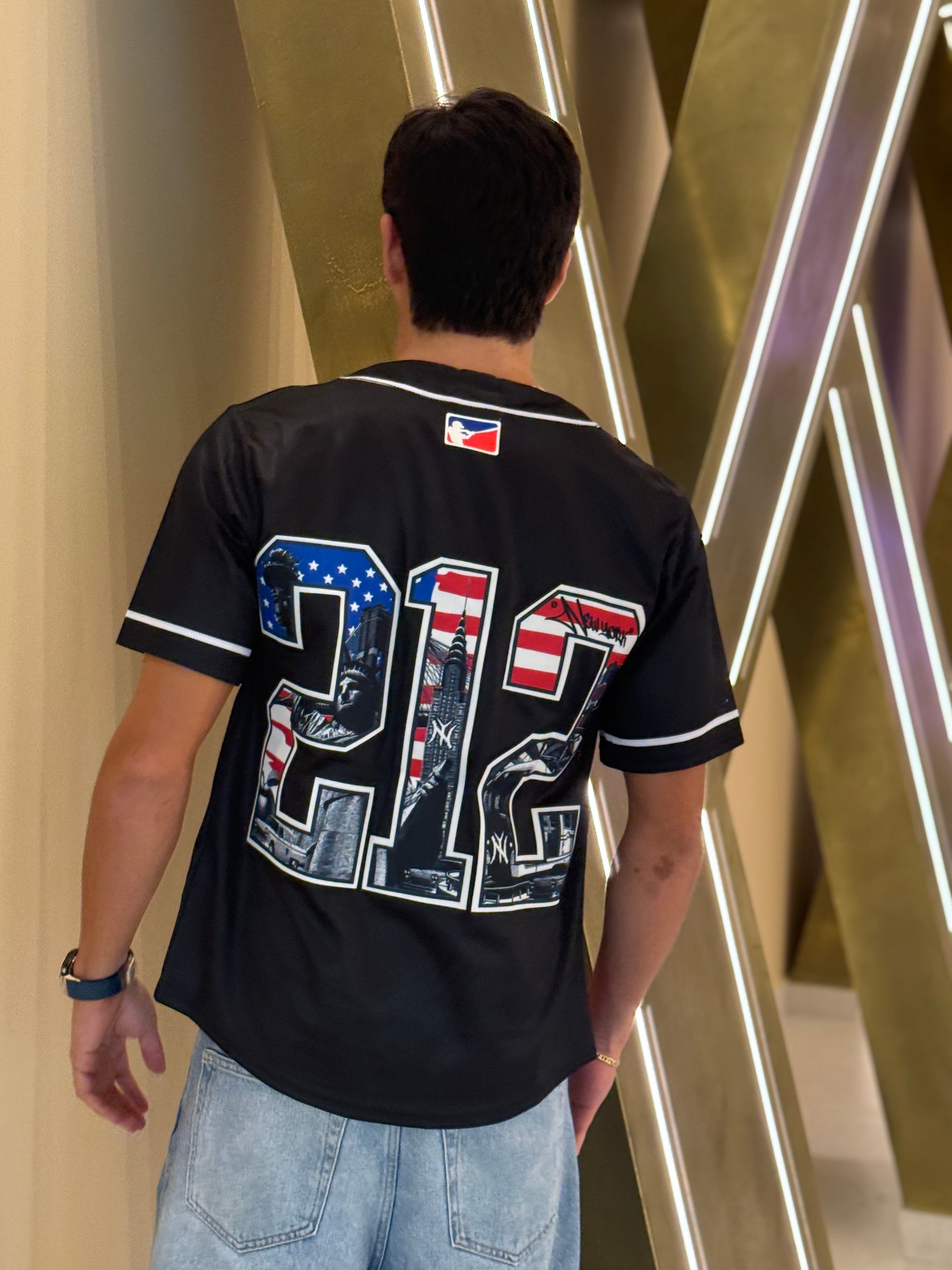 Person wearing a black sports jersey with a unique design, standing in front of a modern architectural background.