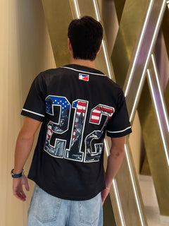 Person wearing a black sports jersey with a unique design, standing in front of a modern architectural background.