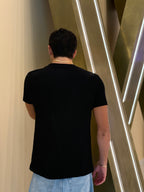 Person wearing a black t-shirt and light blue jeans standing in front of a modern architectural wall.
