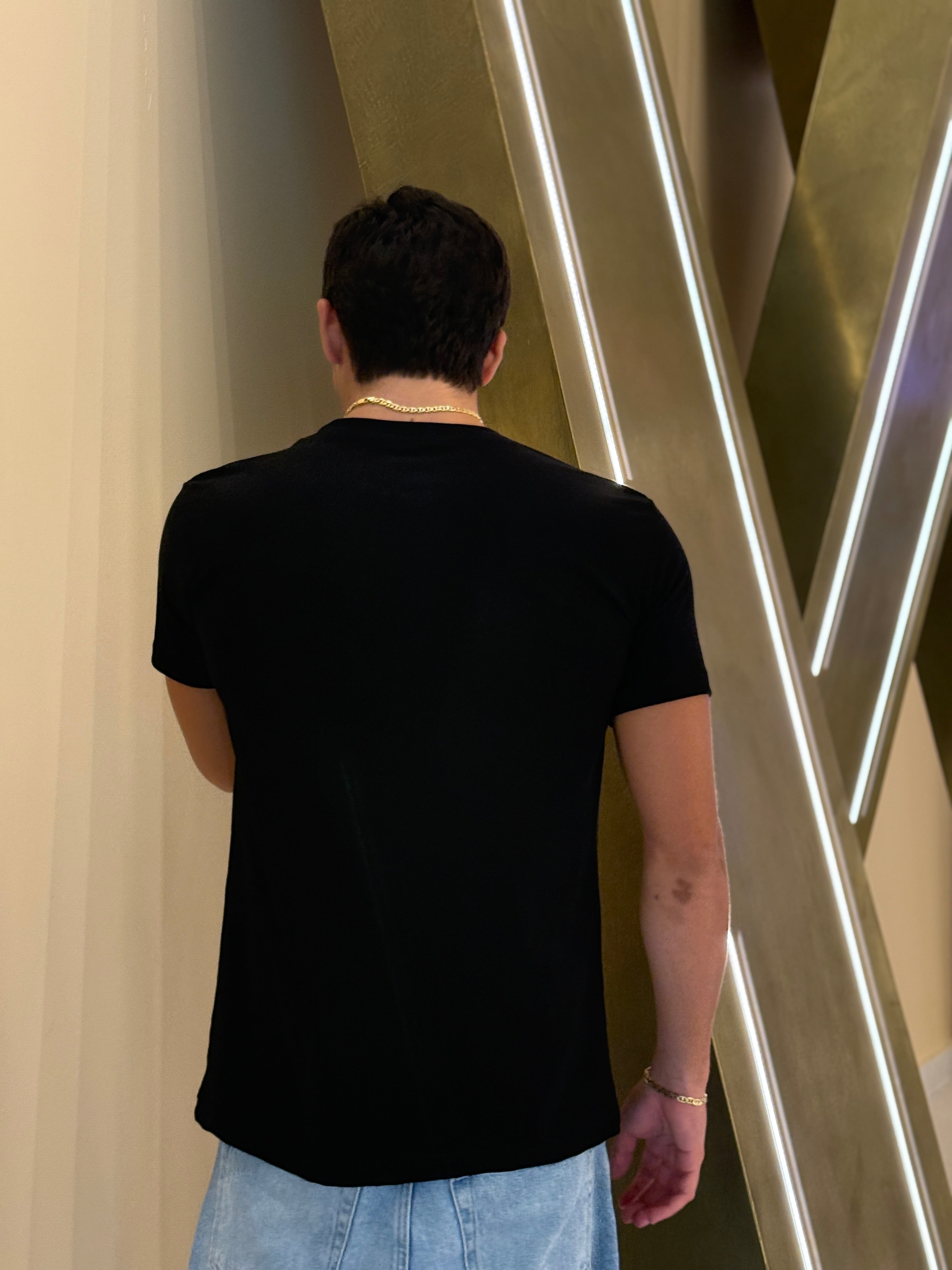 Person wearing a black t-shirt and light blue jeans standing in front of a modern architectural wall.