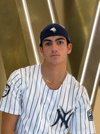 Person wearing a New York Yankees jersey and cap in front of a gold and white abstract background
