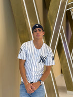 Person wearing a New York Yankees jersey and cap in front of a modern architectural background