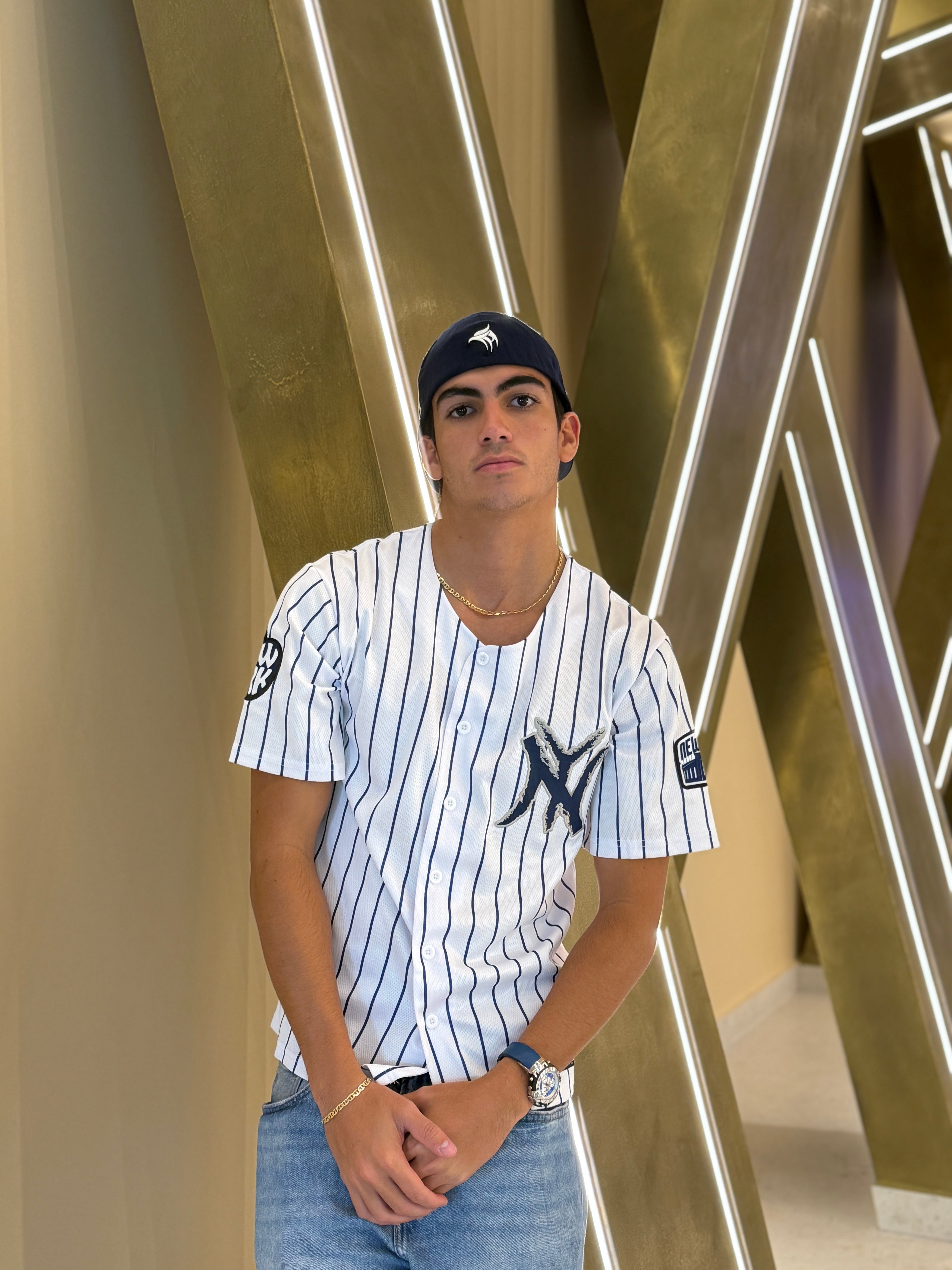 Person wearing a New York Yankees jersey and cap in front of a modern architectural background