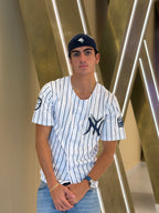 Person wearing a New York Yankees jersey and cap in front of a modern architectural background