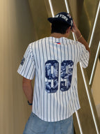 Person wearing a New York Yankees jersey with a cap, standing against a modern interior background.