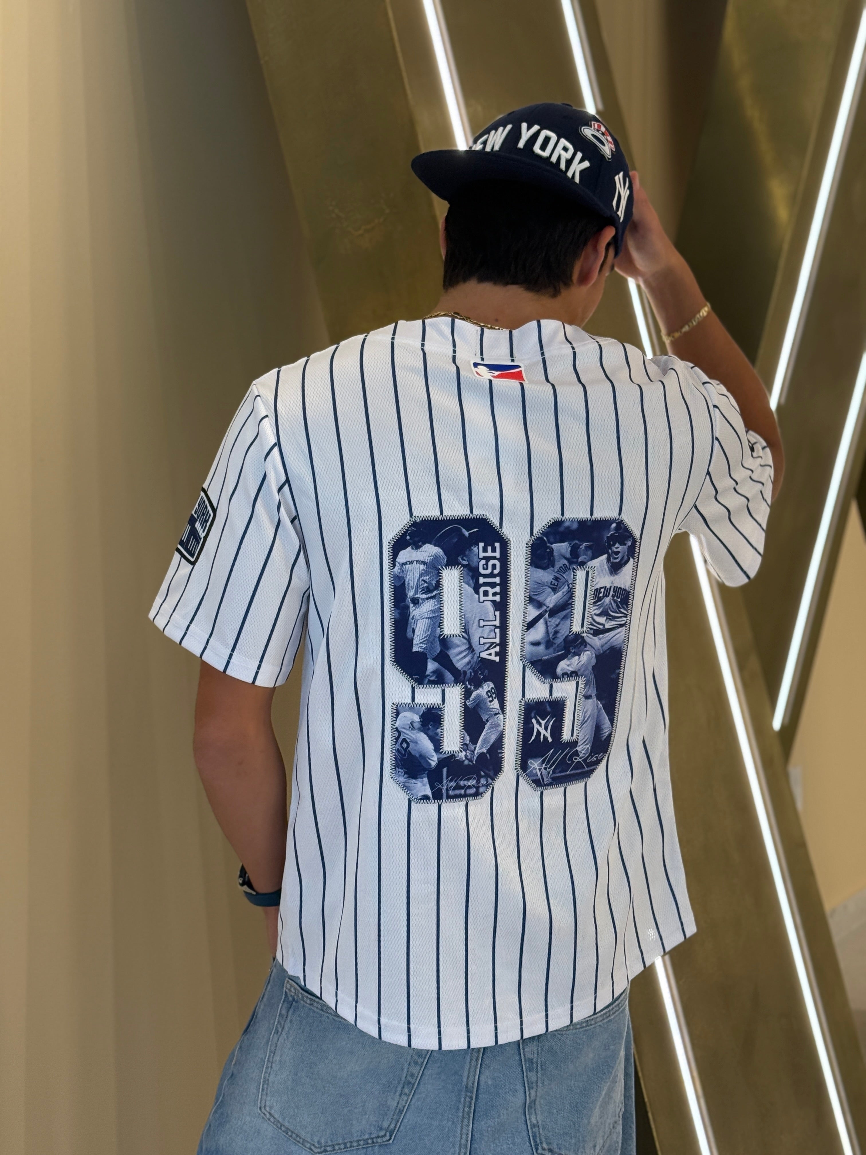 Person wearing a New York Yankees jersey with a cap, standing against a modern interior background.