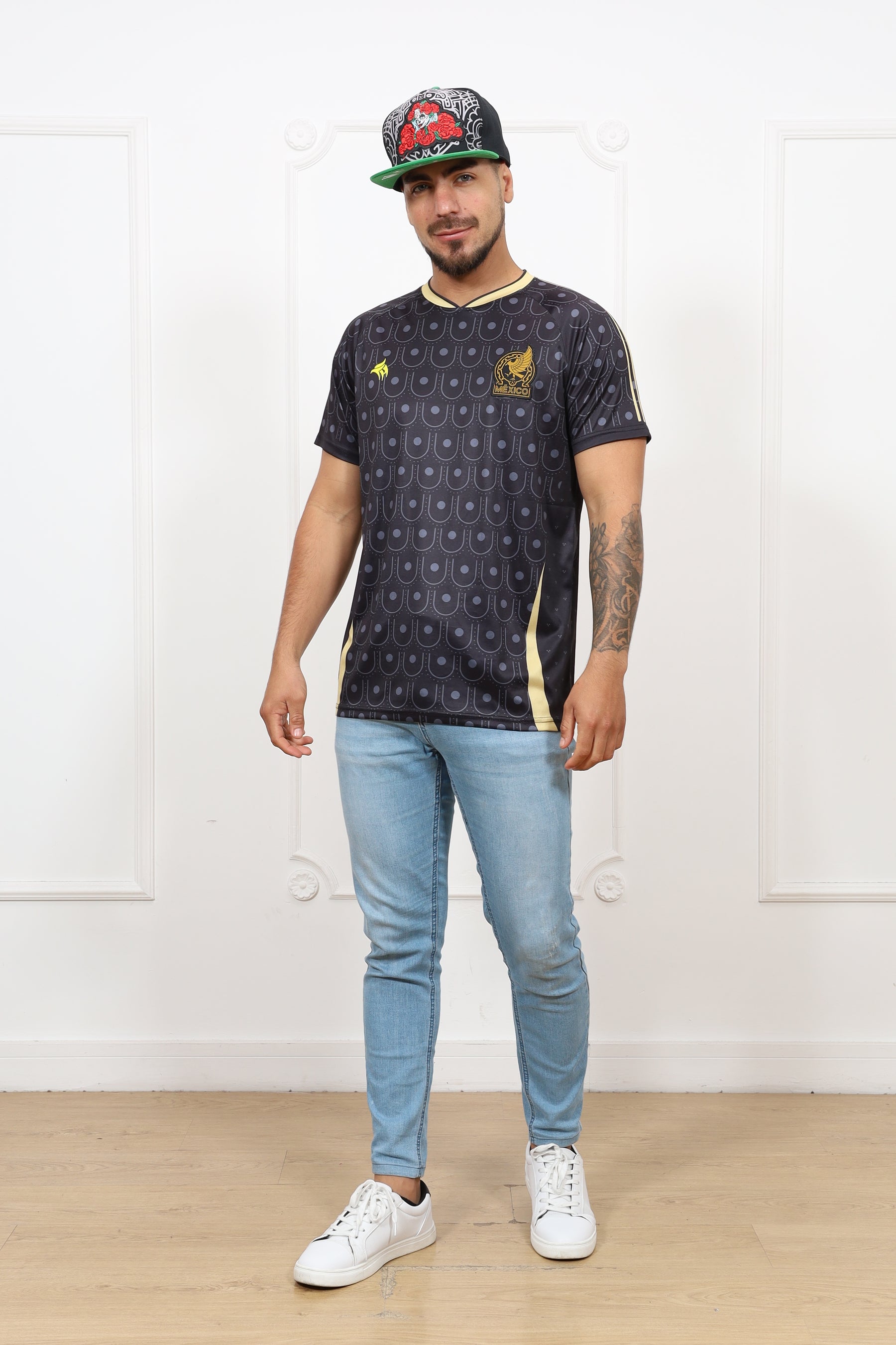 Person wearing a dark patterned shirt with logos, light blue jeans, and white sneakers on a white background.