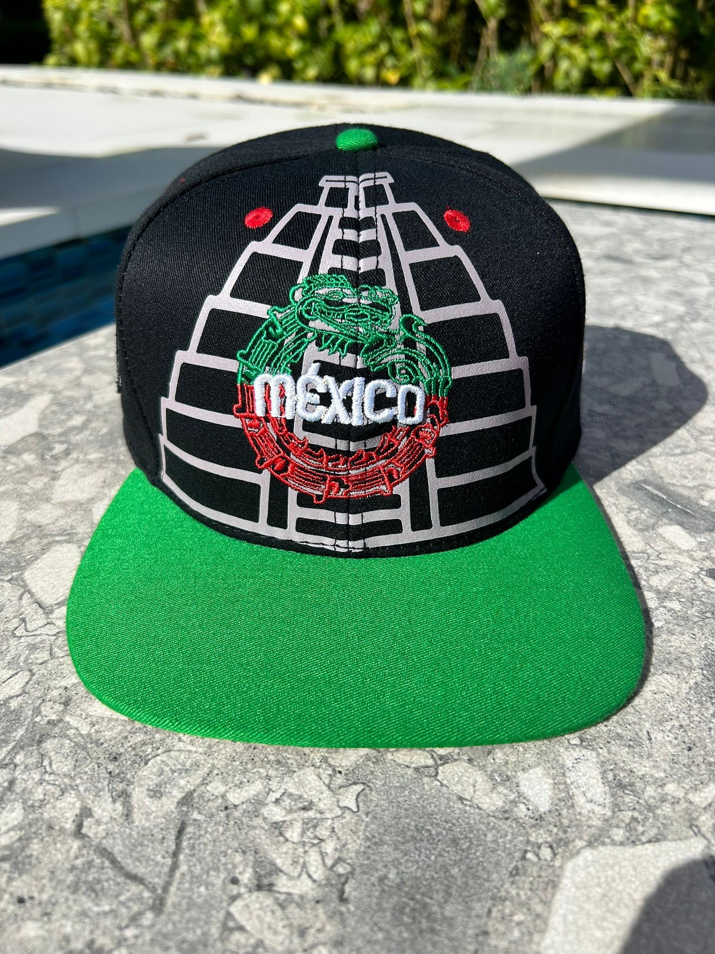 A black structured cap with embroidered Maya pyramids and Quetzalcoatl snake, featuring the Mexican map and coat of arms on the sides, red vent holes, and a flatbill with sublimated symbols.