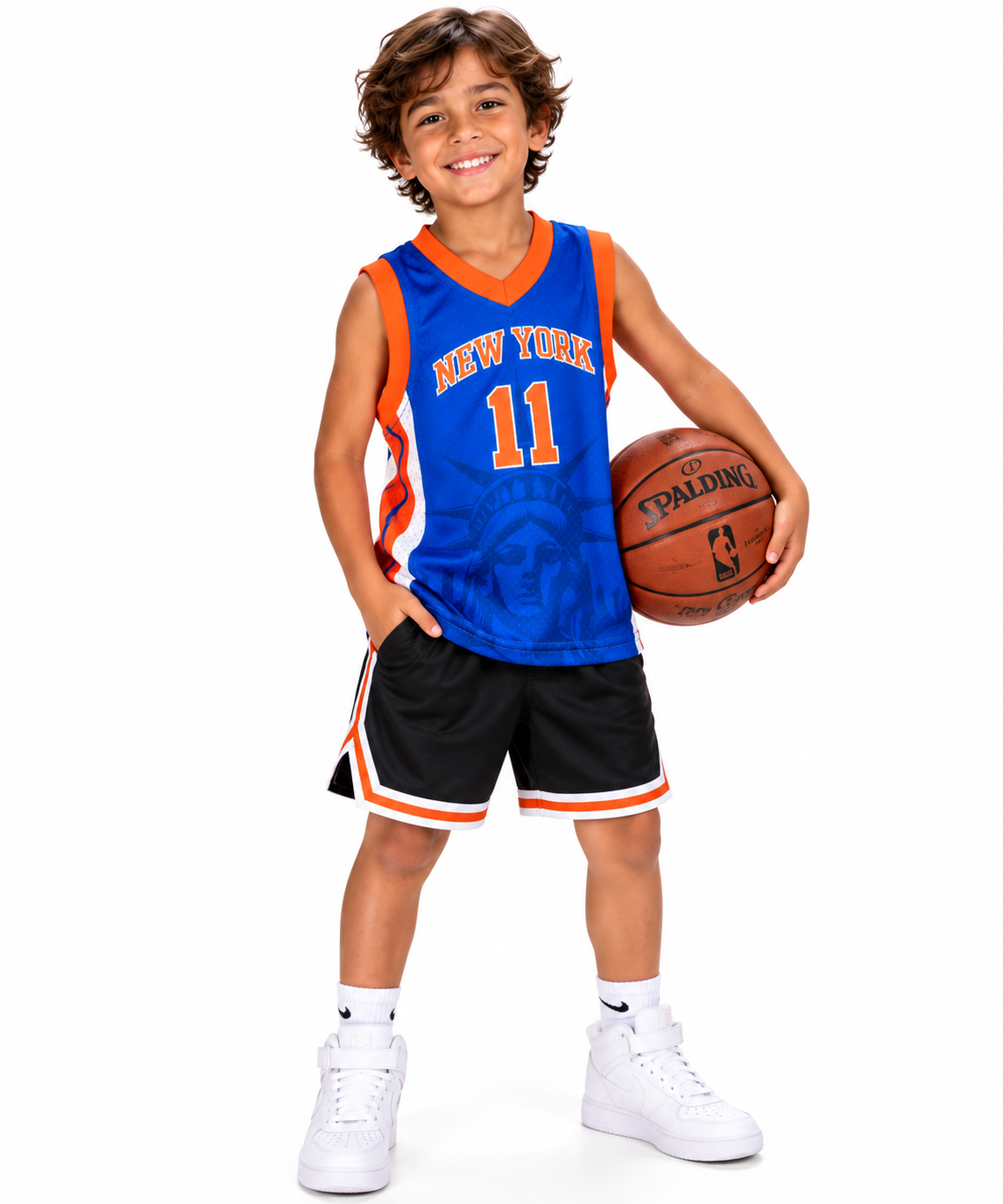 Smiling young boy wearing the blue New York 11 kids basketball jersey with orange number 11, black shorts and white sneakers, holding a basketball on a white studio background