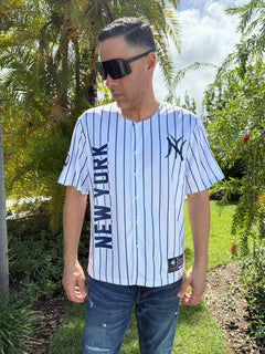 Man wearing a New York Yankees jersey outdoors with greenery in the background