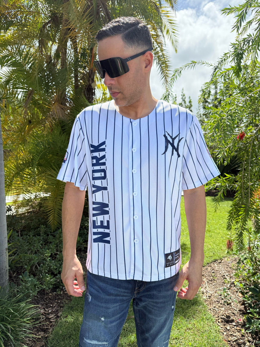 Man wearing a New York Yankees jersey outdoors with greenery in the background
