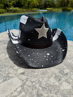 Black cowboy hat with a star design on a stone surface near a pool.