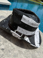 Black and white patterned hat with a black band on a concrete surface near a pool.