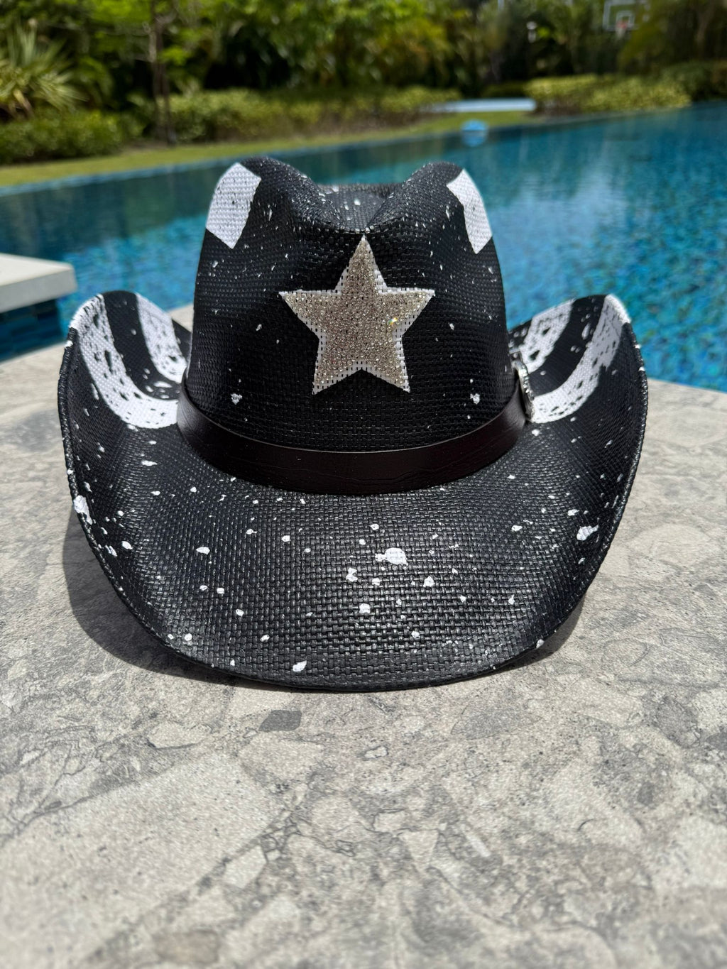 Black cowboy hat with white star design on a stone surface near a pool.