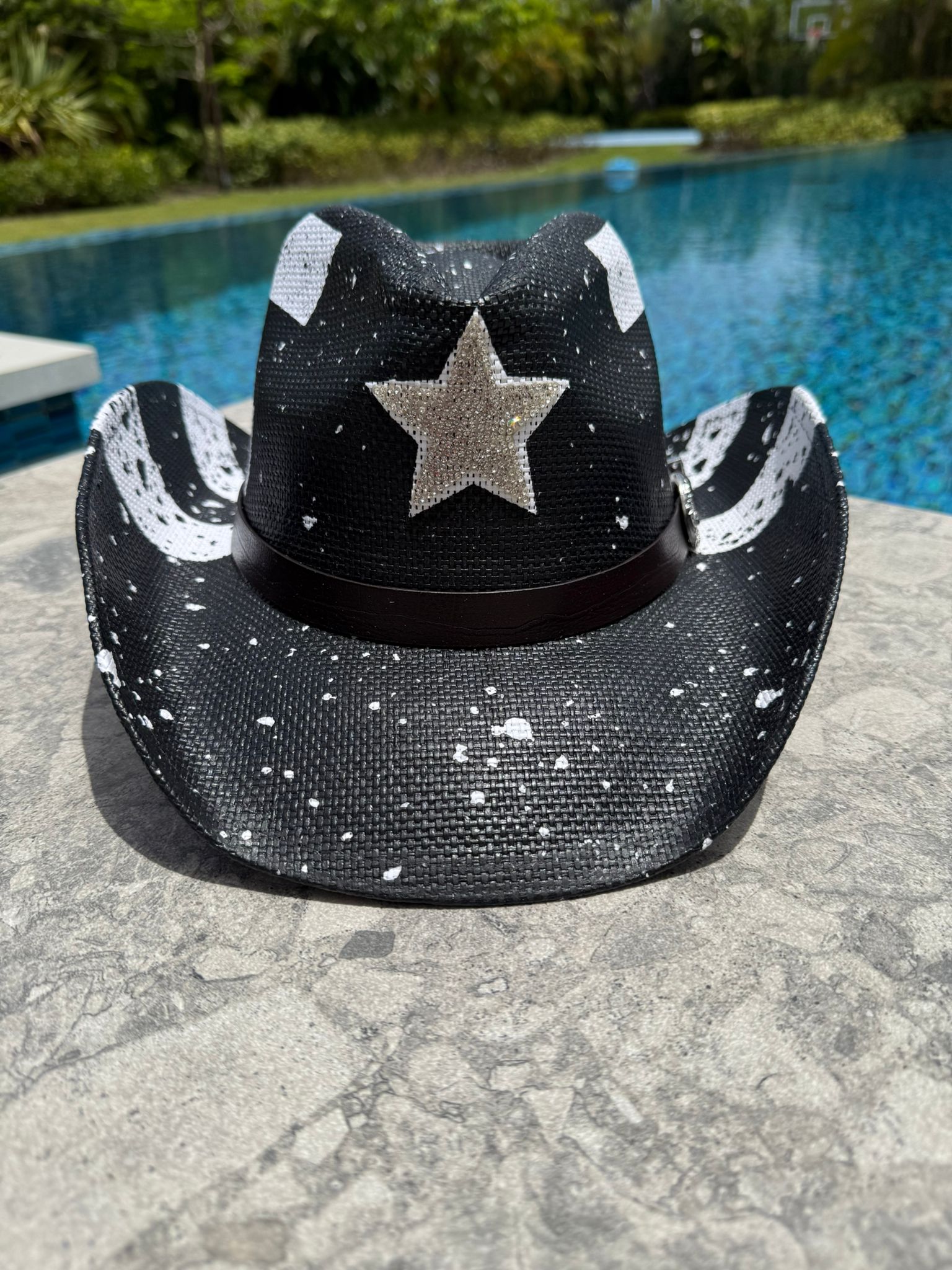 Black cowboy hat with white star design on a stone surface near a pool.