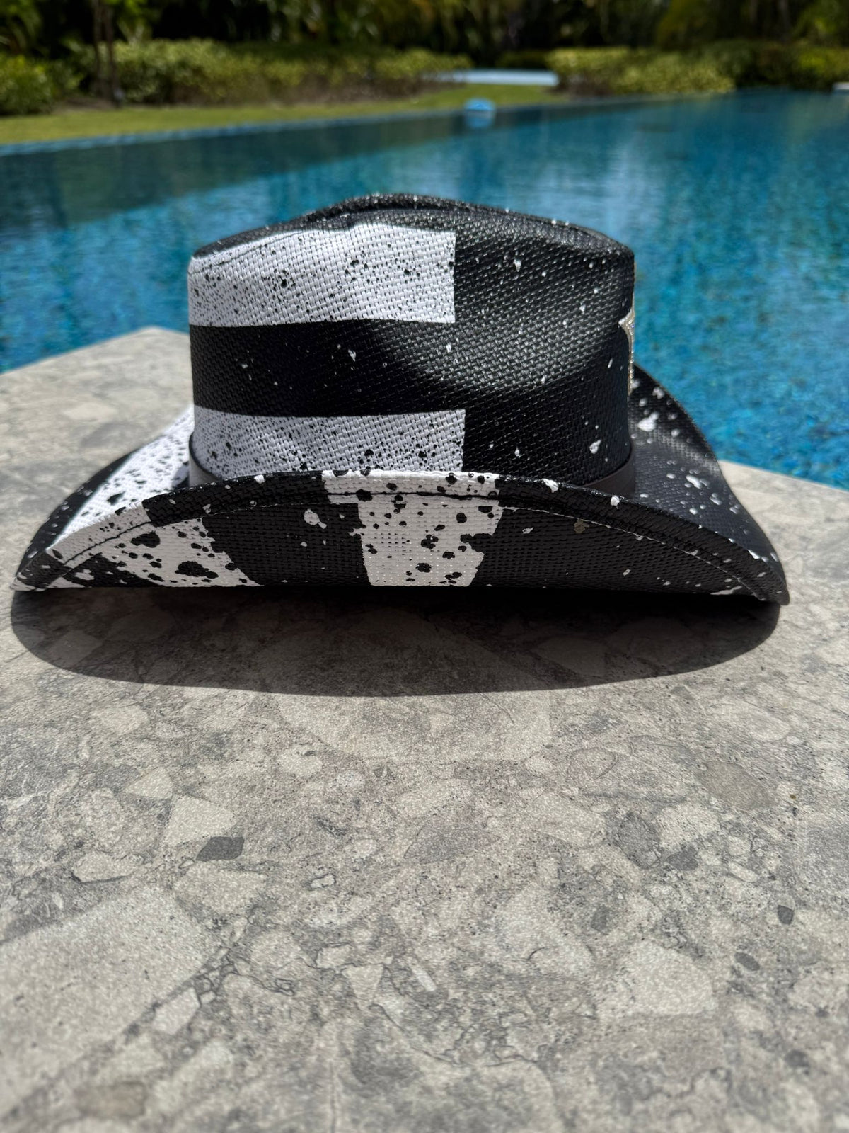 Black and white patterned hat on a stone surface with a pool in the background