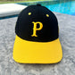 A black and yellow baseball cap with a 3D embroidered 'P' on the front and '21' on the side, with Clemente's name on the back and a yellow curved brim with 'GOAT' underneath.