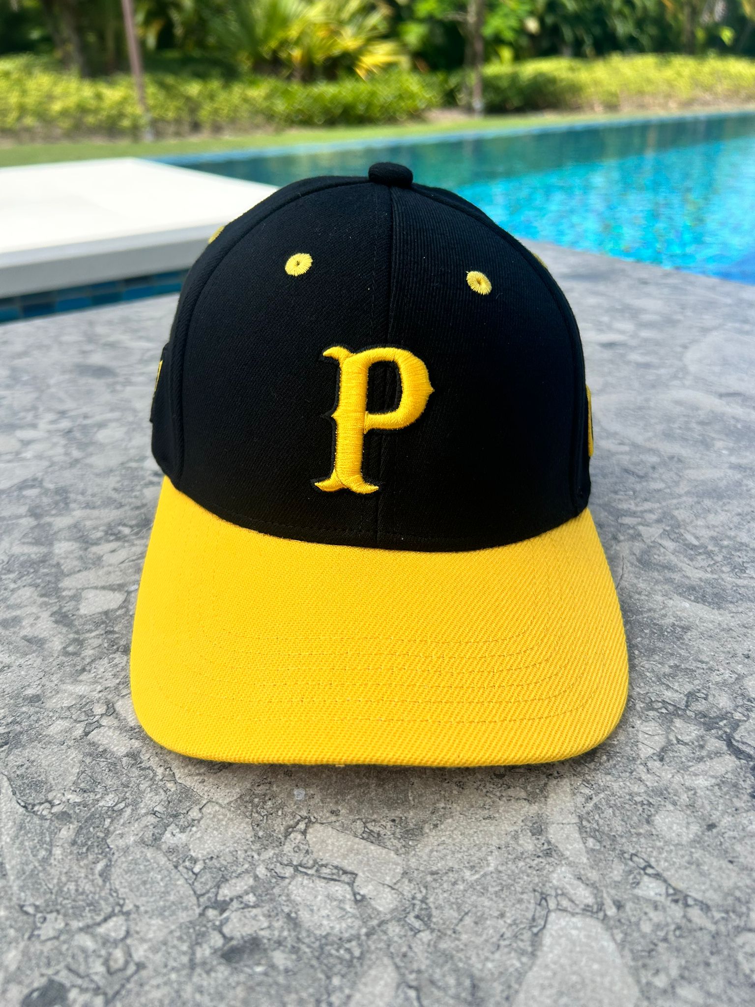 A black and yellow baseball cap with a 3D embroidered 'P' on the front and '21' on the side, with Clemente's name on the back and a yellow curved brim with 'GOAT' underneath. Main image