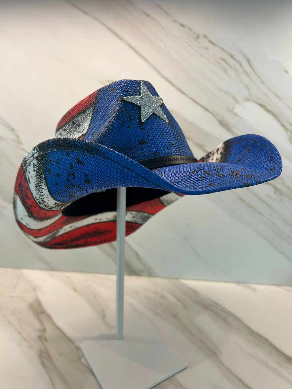 Colorful cowboy hat with star design on a stand against a marble background