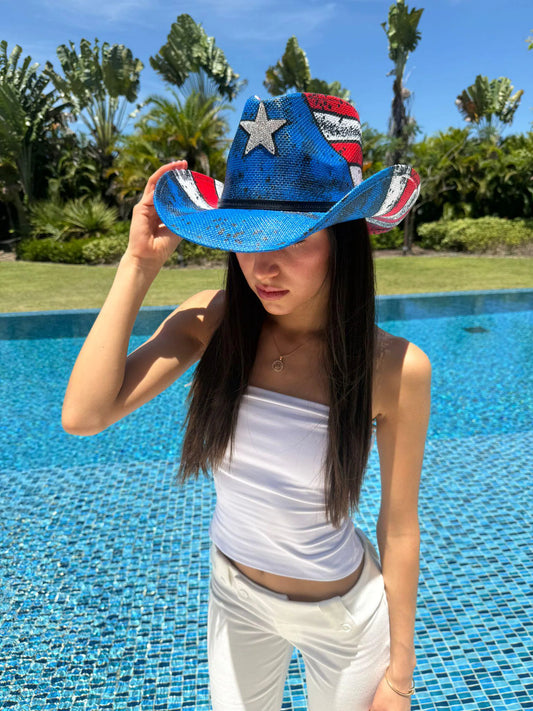 Person wearing a blue cowboy hat with American flag design by a pool