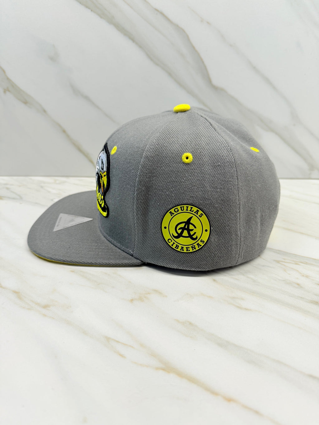 Side view showing Águilas Cibaeñas logo patch on gray snapback cap

