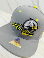A grey and yellow flatbill snapback cap with an embroidered eagle logo on the front, resembling a baseball cap.