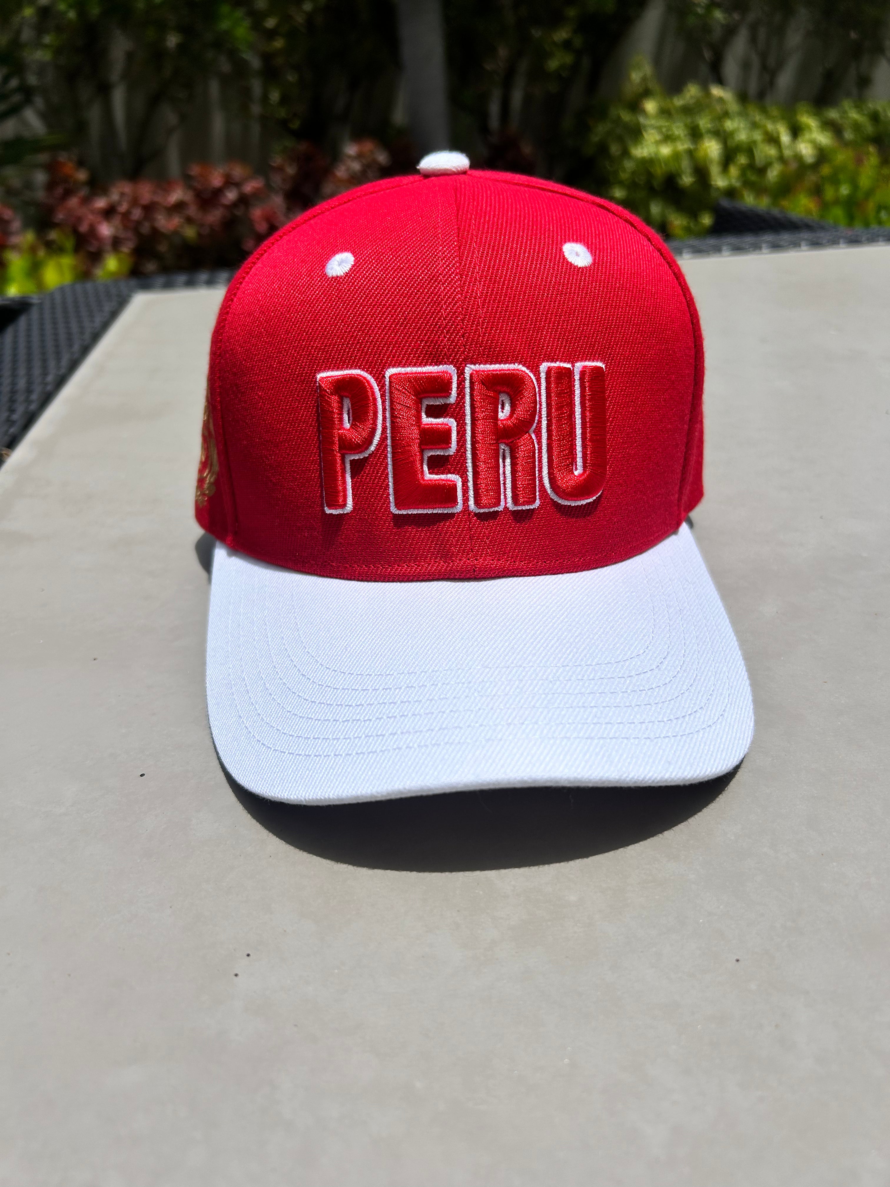 A red and white baseball cap with 'PERU' embroidered in 3D on the front and the Coat of Arms of Peru on the sides, displayed on a flat surface.